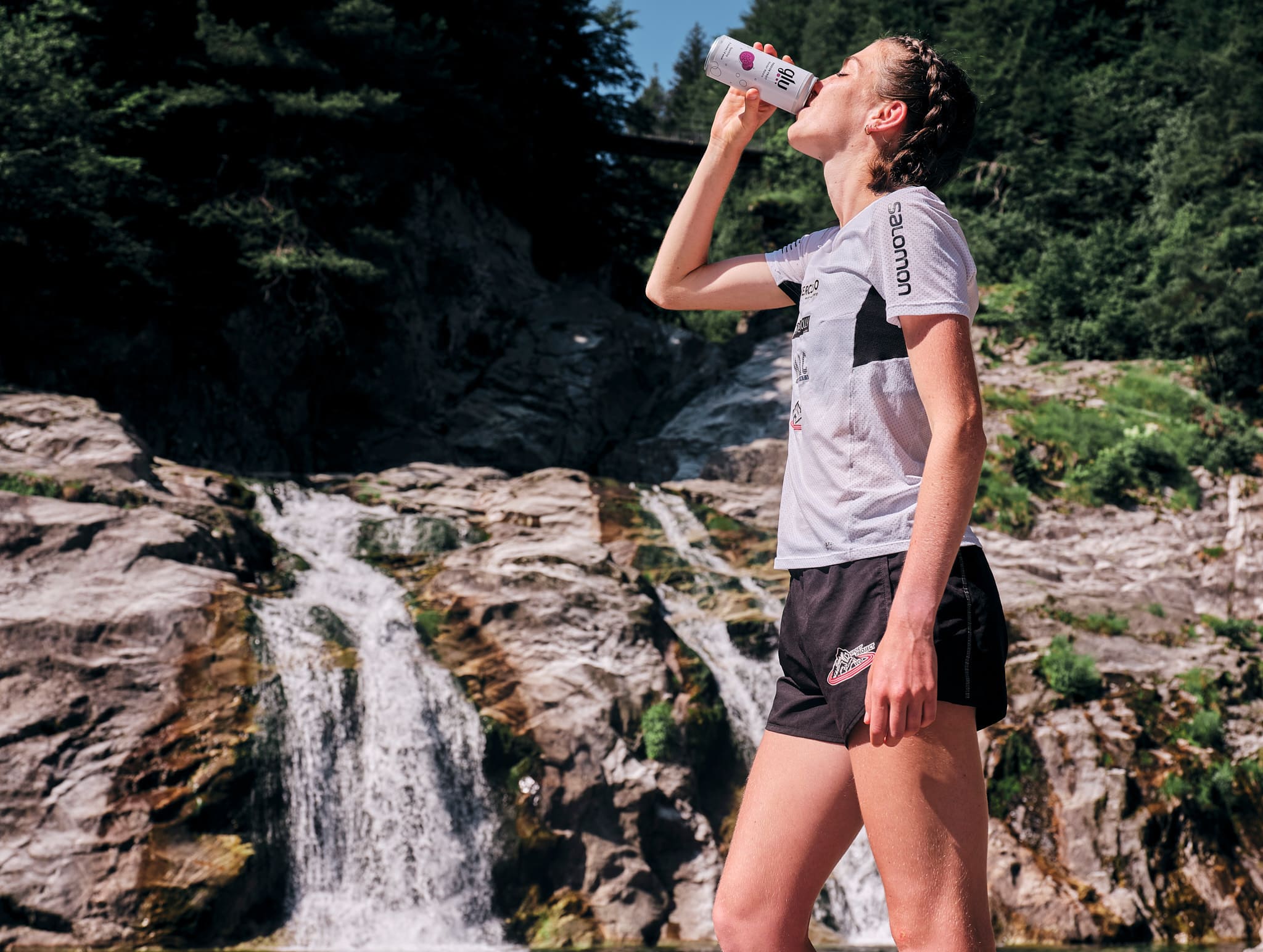 Ragazza beve Glu Passion Fruit dopo una camminata in montagna, a bordo di una piccola cascata